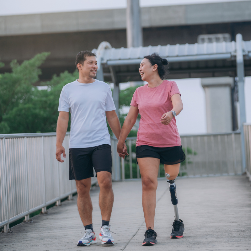 A couple walking together and laughing - holding hands on a bridge, the woman wearing a prosthetic leg
